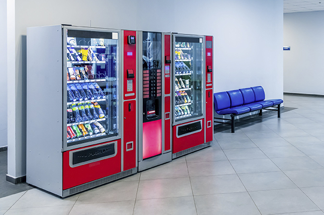 Group of red vending machines stands by the wall inside public building. No people. Unmanned store. Copy space for your text. Small business theme.